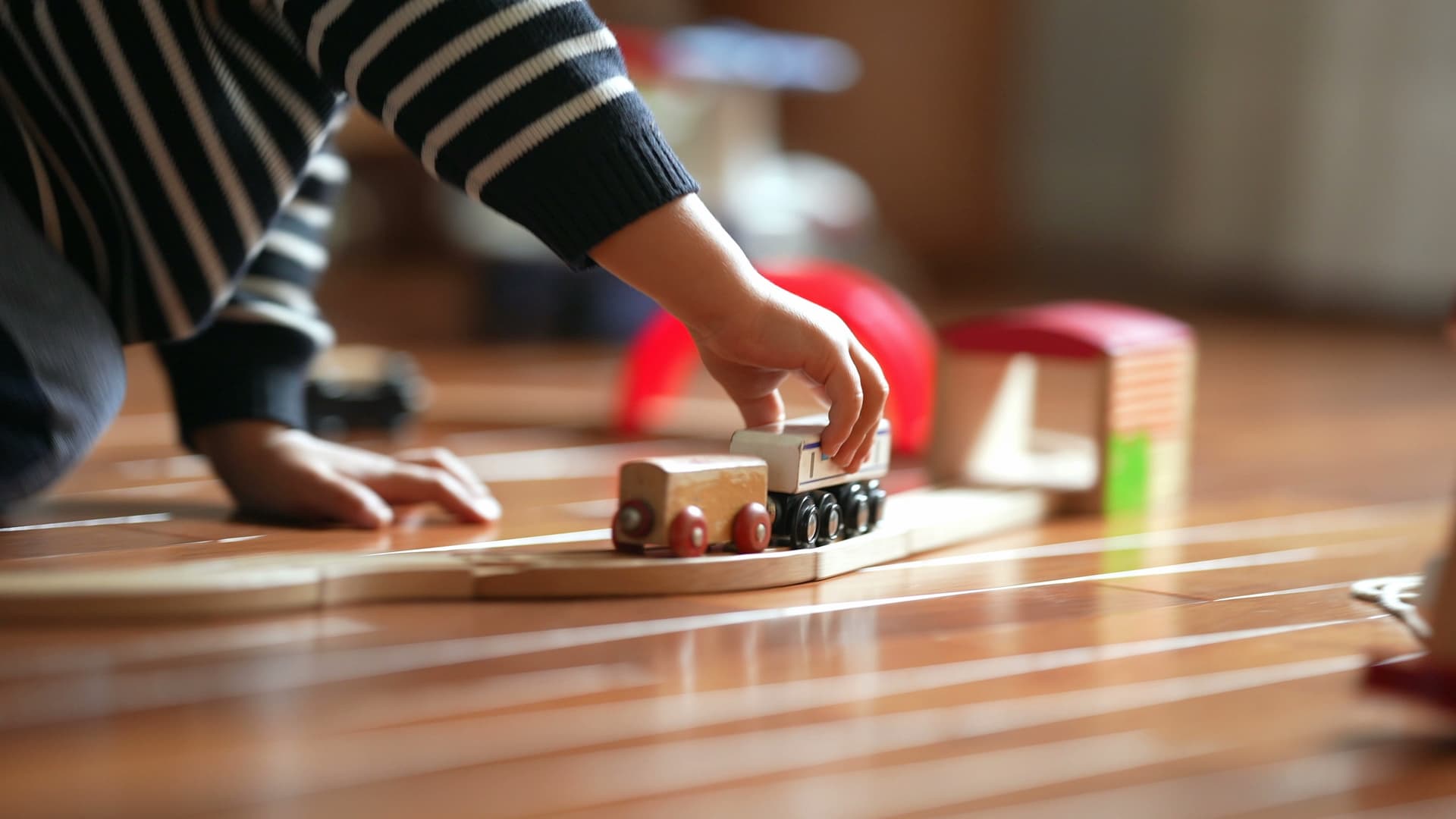 A toddler's hand pushes a wooden toy train along a track on a wooden floor