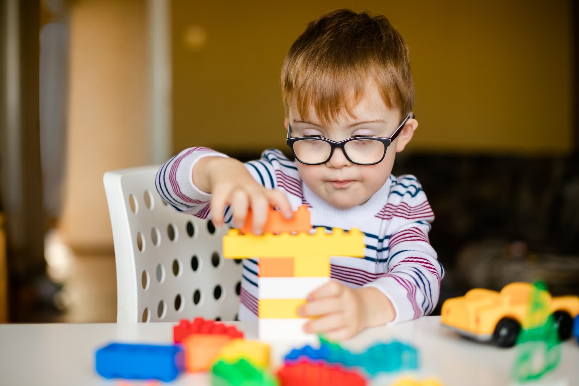 A young boy wearing glasses concentrates while building a tower out of toy blocks